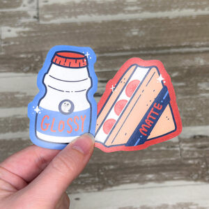 hand holding two die cut stickers printed on glossy and matte sticker papers